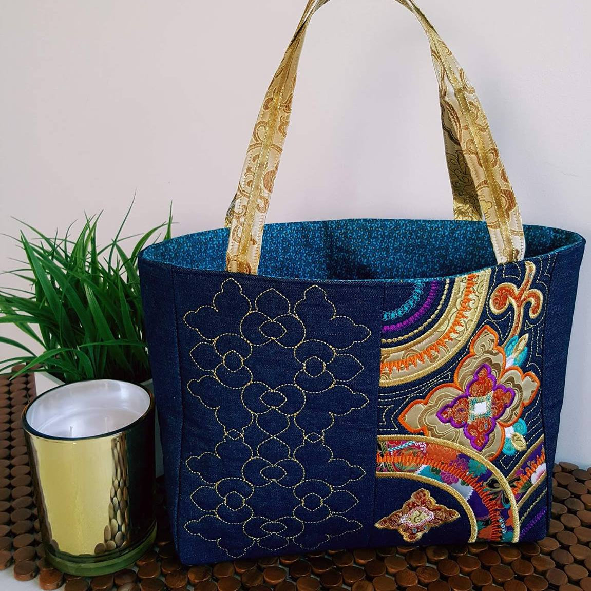 Blue embroidered tote bag with colorful floral design styled with a plant and candle