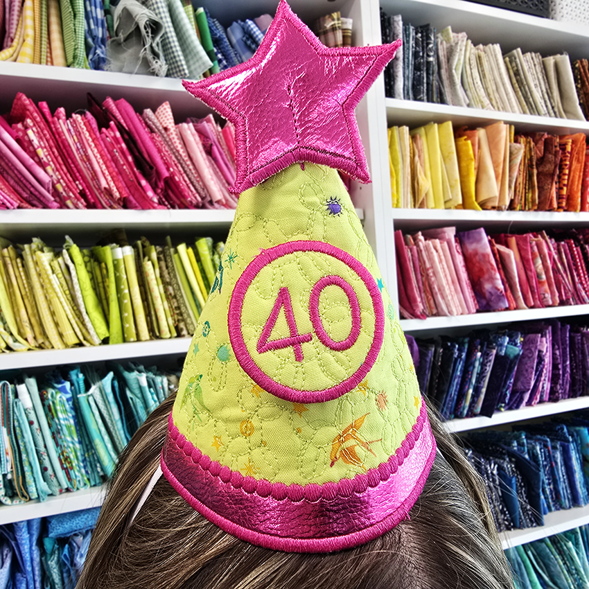 Person wearing ITH party hat with a star and 40 in front of shelves filled with fabric at sweet pea hq
