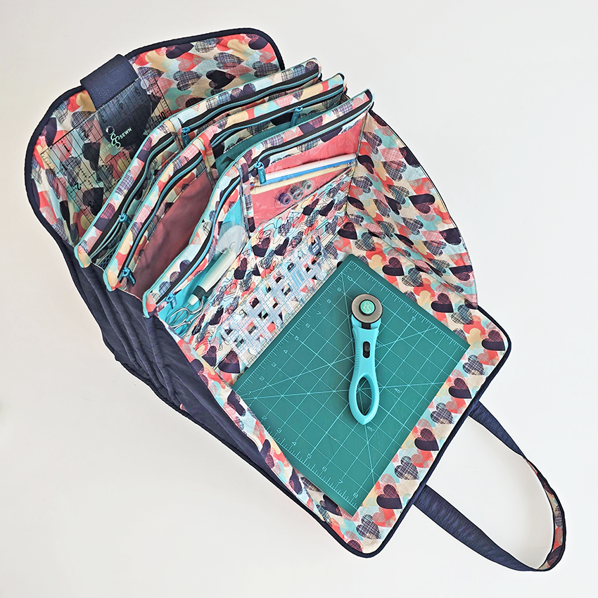 Multicolored patterned roll-up craft tote bag with a cutting mat and rotary cutter on a white background