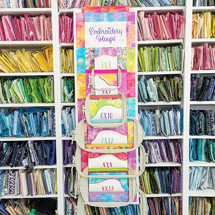 Embroidery hoops organizer with colorful labels against a backdrop of fabric shelves.