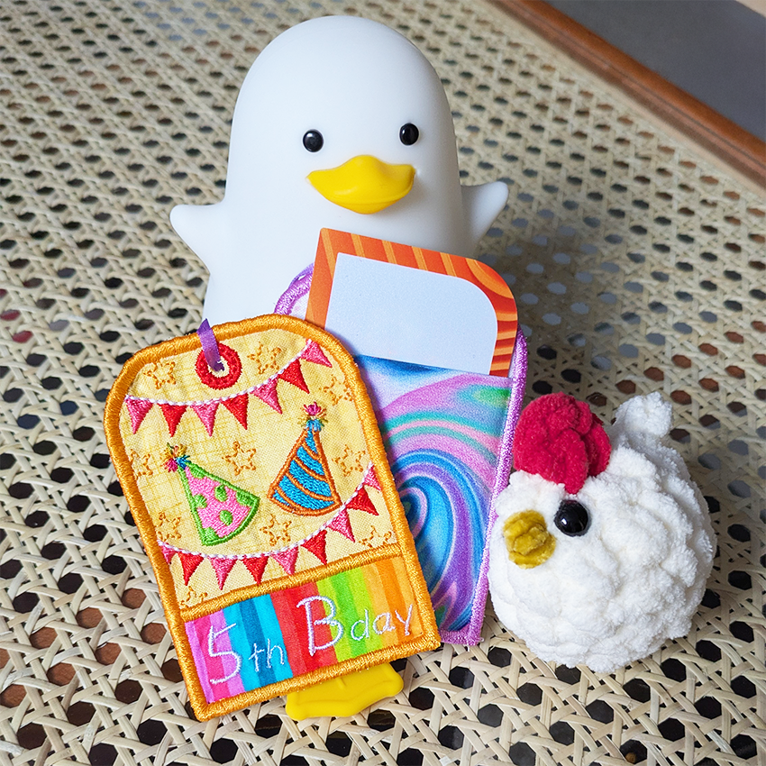 White duck toy holding a colorful card with a chicken toy on a textured surface
