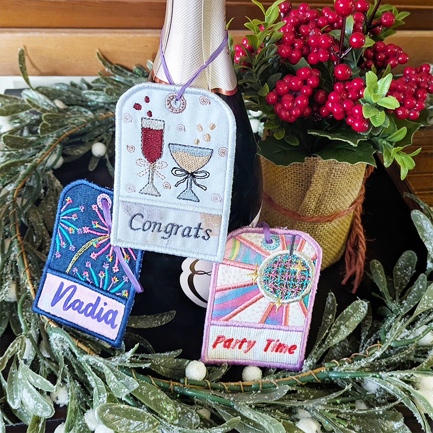 Decorative gift tags with embroidered designs on a green wreath with berries.