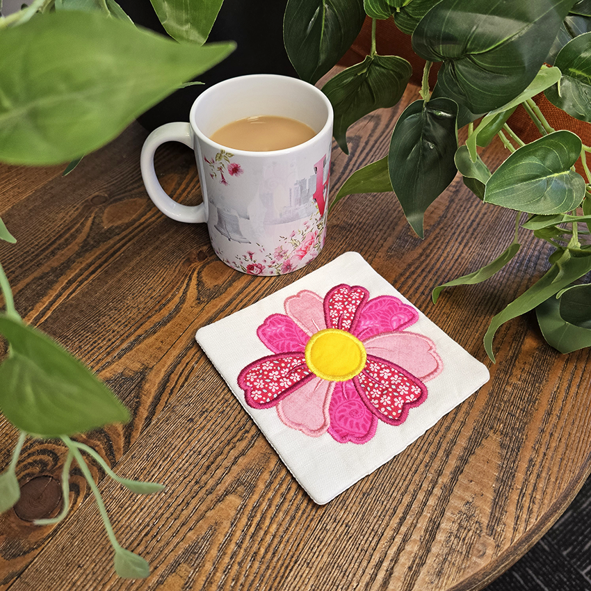 Mug with floral design on a wooden table next to a pink flower coaster