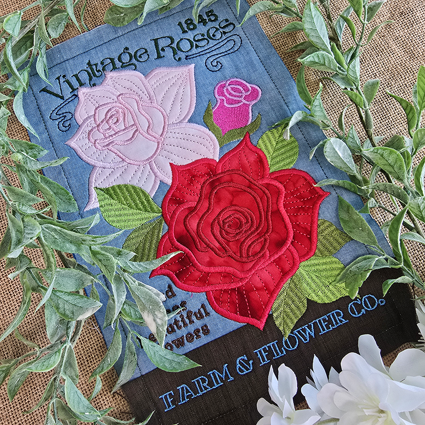 Embroidered patch with red and pink roses on a blue background, surrounded by green leaves.
