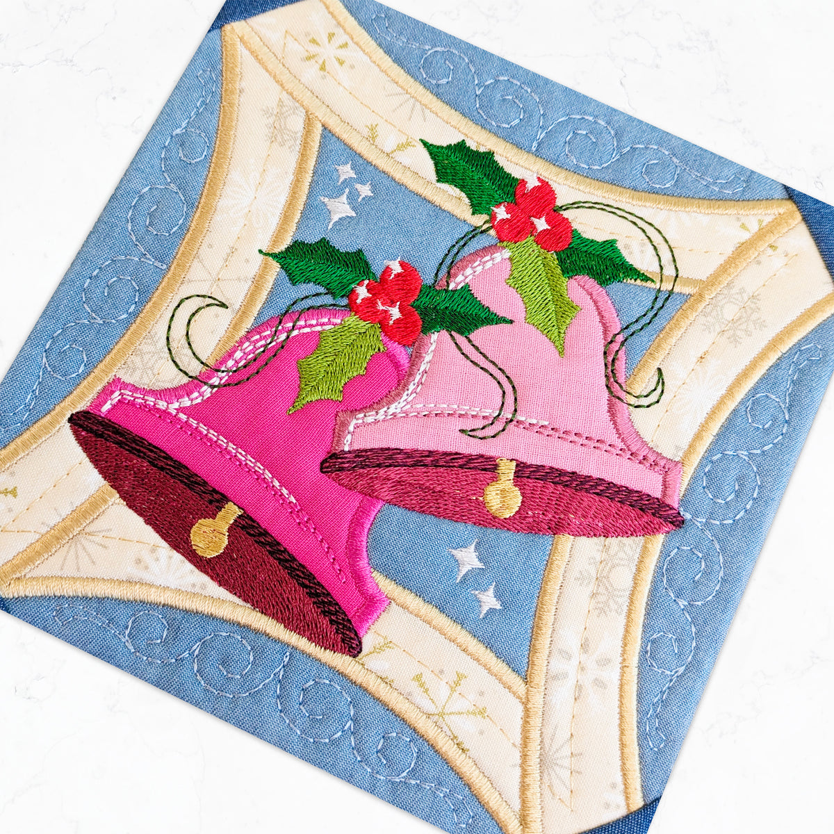 Close up quilted fabric panel featuring two pink Christmas bells with green holly leaves and red berries made by sweet pea