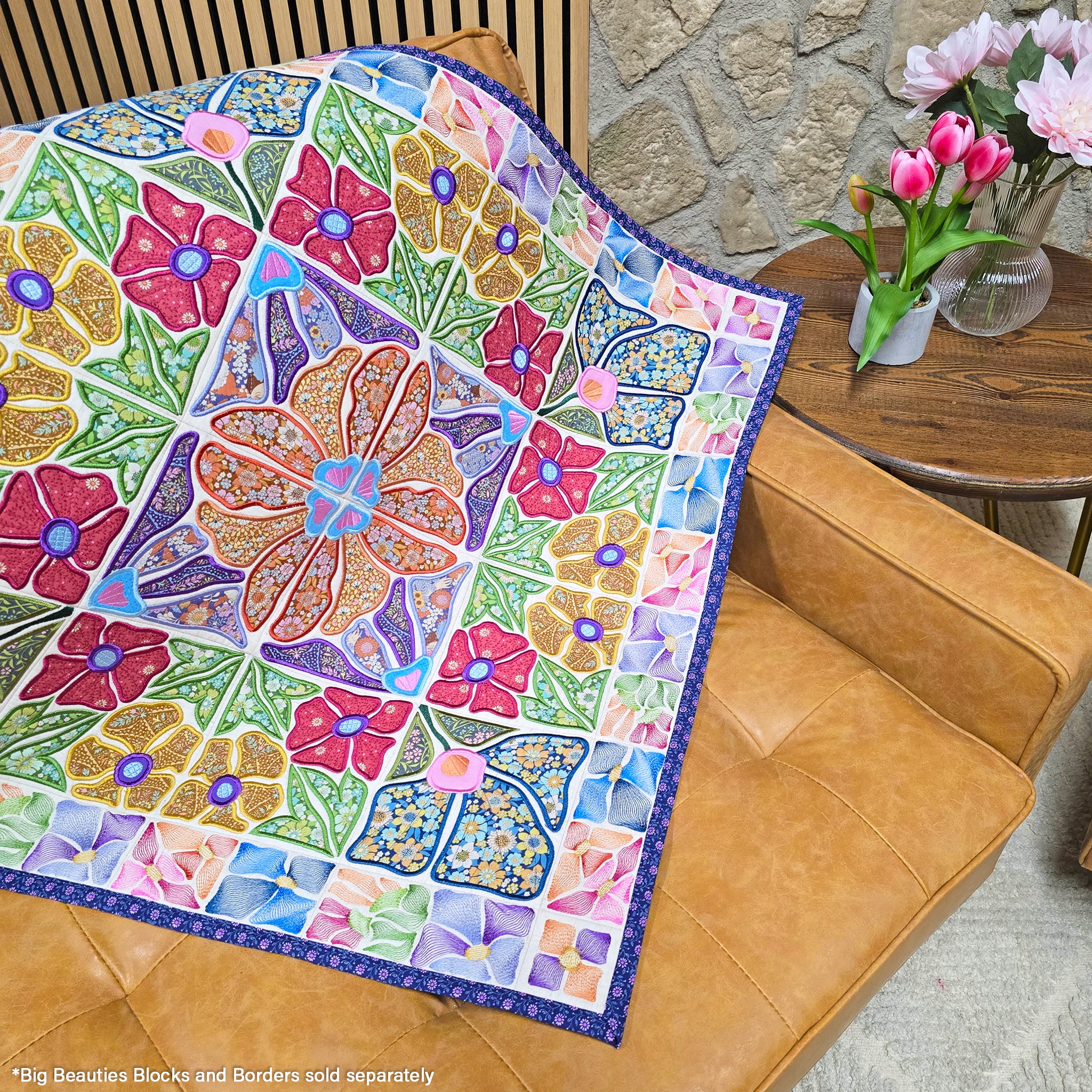 Colorful ITH floral quilt on a brown couch with a stone wall and table in the background.