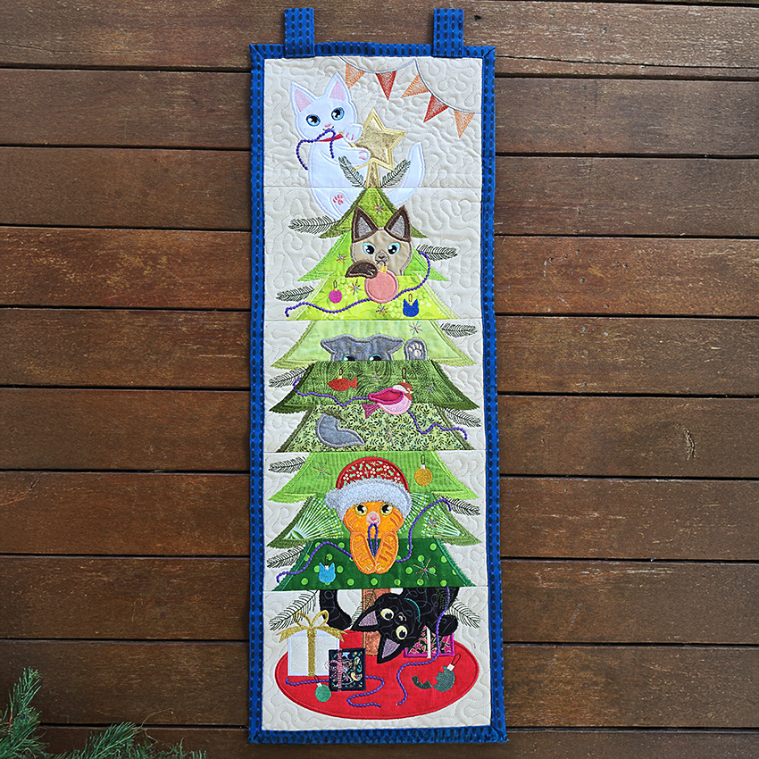 Embroidered wall hanging with a Christmas tree design featuring animals on a wooden background
