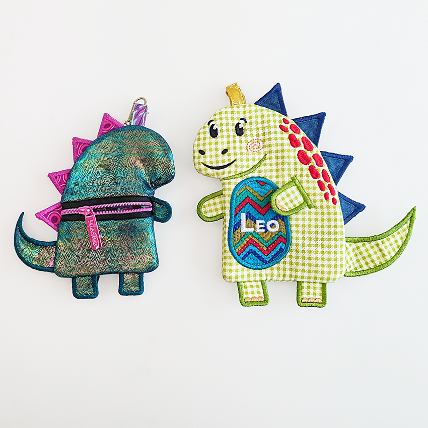 shiny dinosaur purse with pink spikes from the back, next to green dinosaur with custom text in bigger size