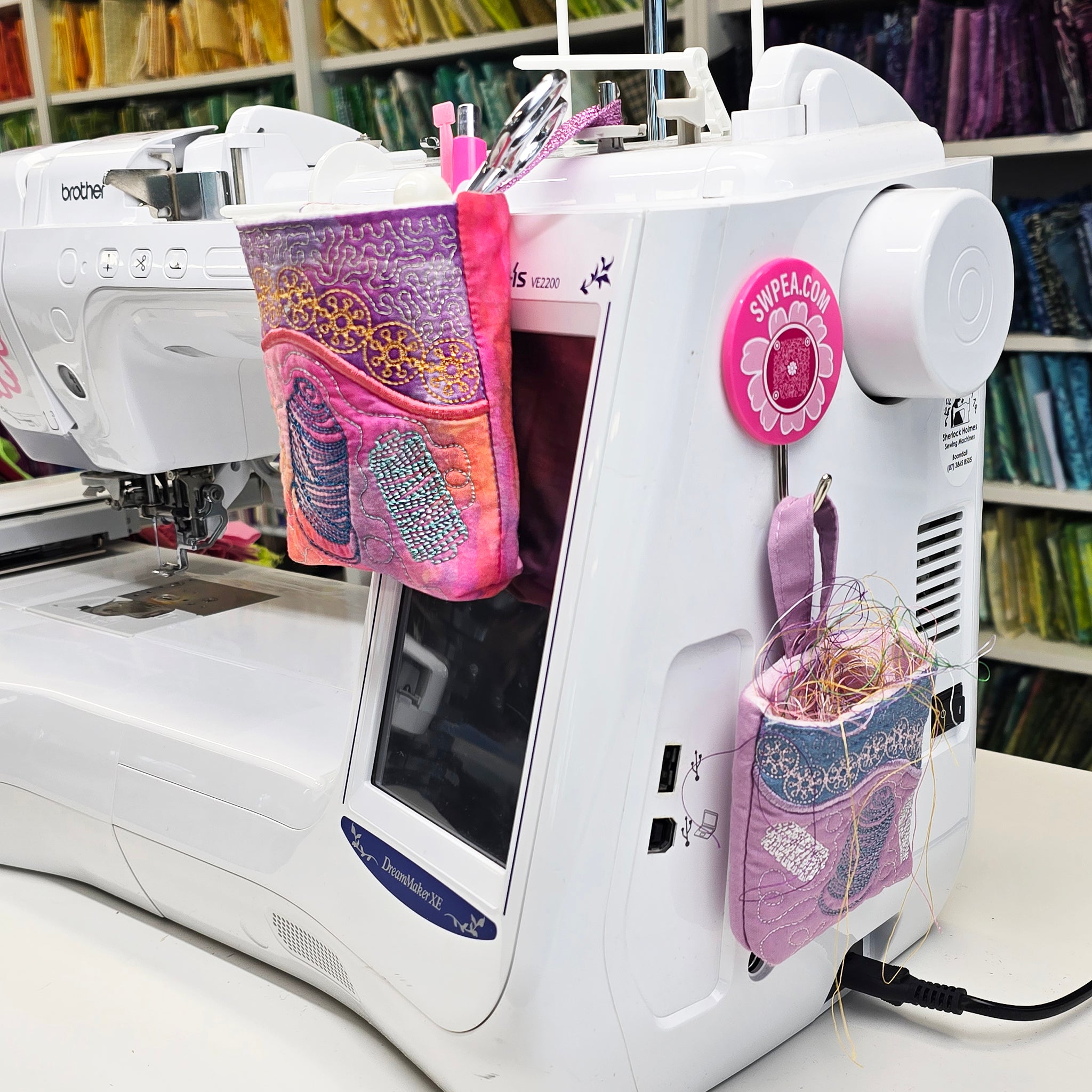 two sizes of the hanging thread catcher on an embroidery machine hooked into a bobbin holder and a sweet pea hook