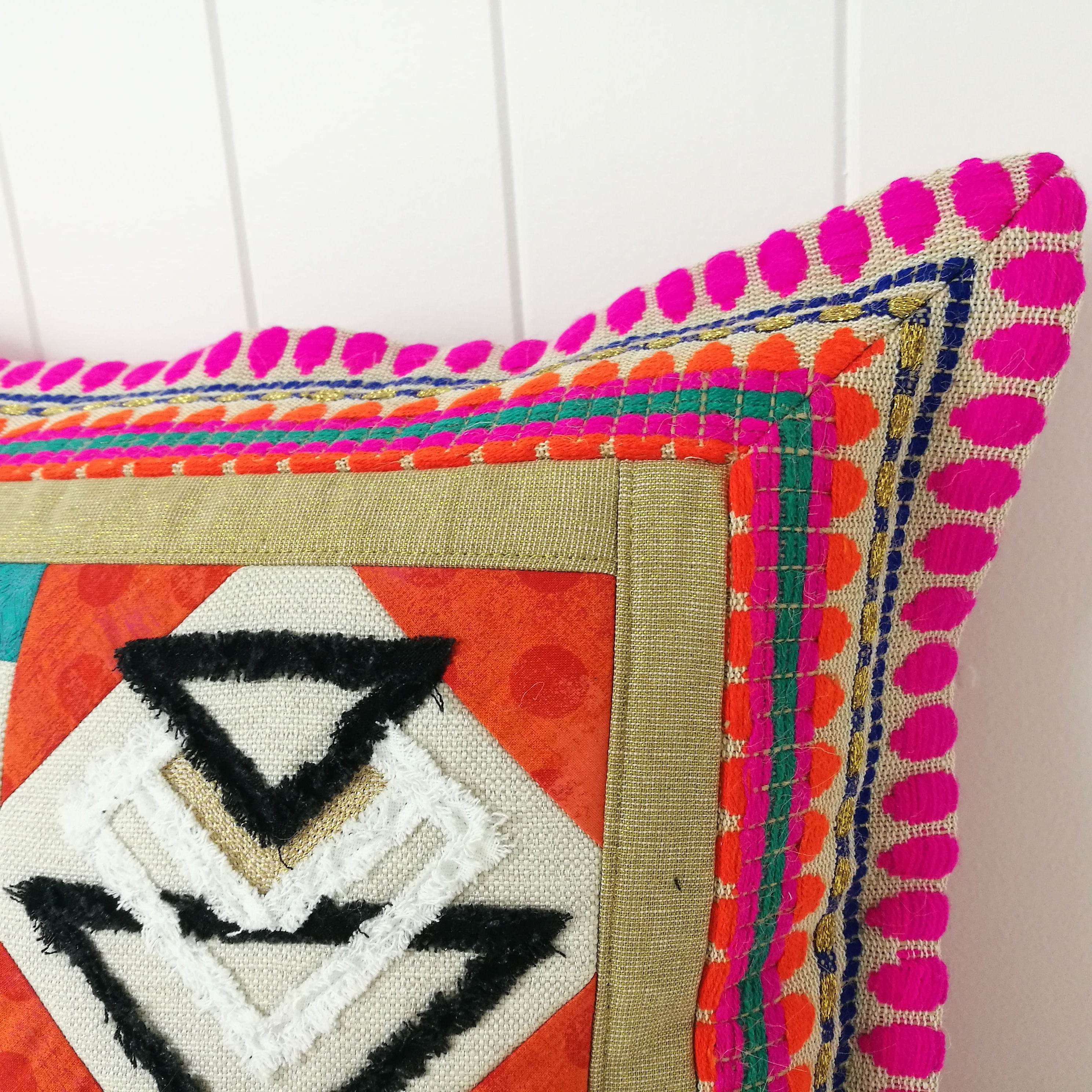 Colorful embroidered pillow with geometric patterns on a white background