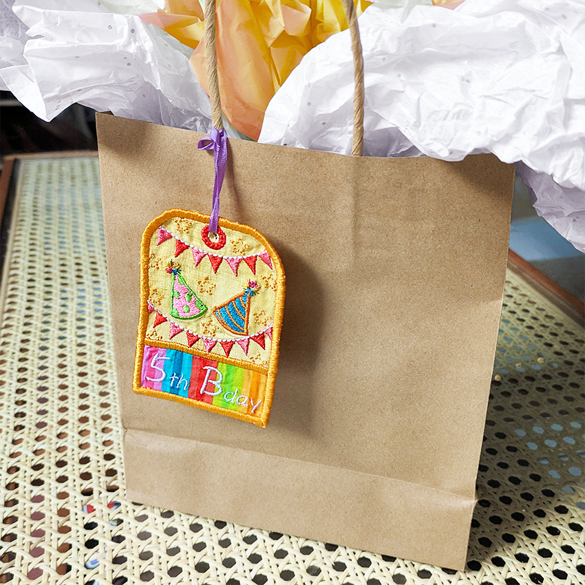 Colorful '5th Birthday' patch on a brown paper bag with a textured surface background.